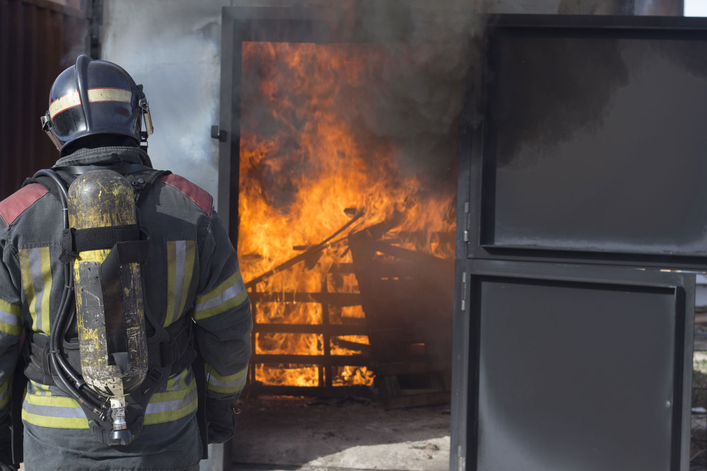 Brannmann i uniform med ryggen til kamera ser på flammer i et hus