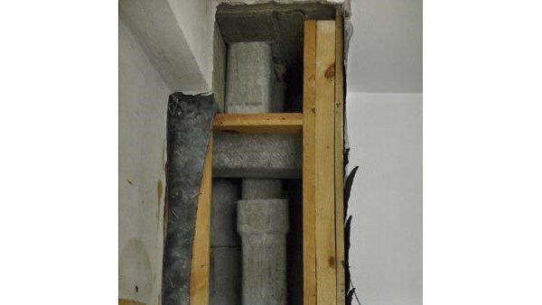 Bildet viser en vegg der gipsplatene er fjernet fra bindingsverket. Bak bindingsverket er det både en vertikal og en horisontal ventilasjonskanal som er laget av grå eternitt.
