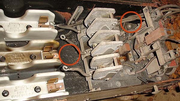 Bildet viser en elektrisk installasjon: Bakelittplate armert med asbest i bakkant for gnistvern og gamle kabler isolert med asbestholdig materiale.