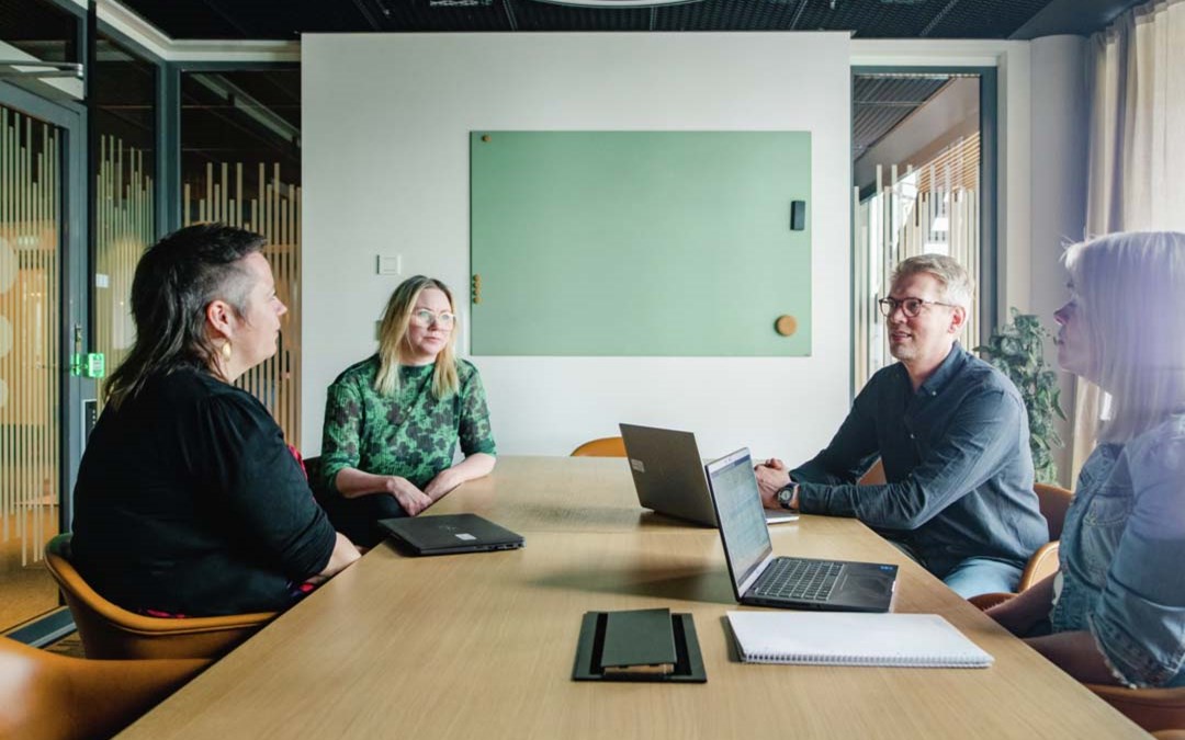 Fire personer sitter rundt et bord i et møterom.
