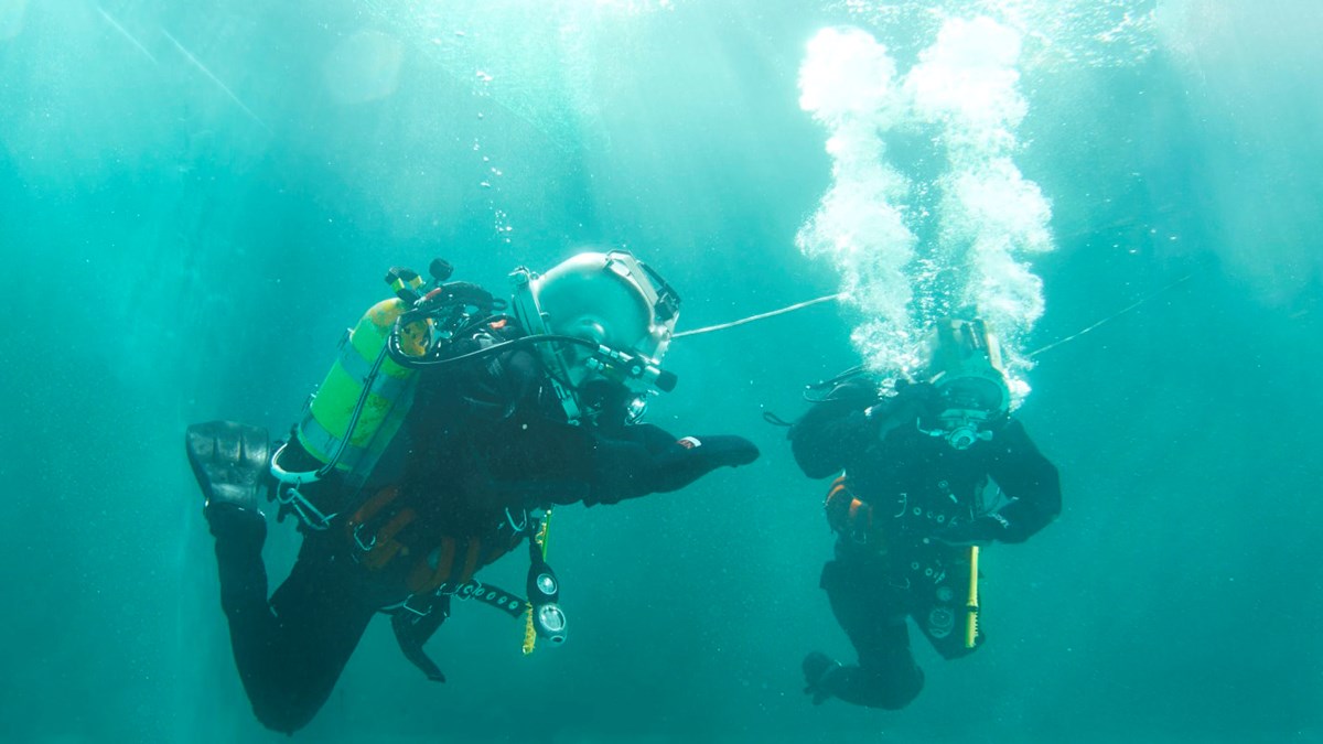 To arbeidsdykkere under vann med oksygentanker og hjelmer 