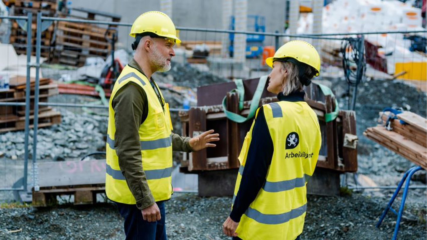 Kvinne og mann i et rom rundt et bord mens hun noterer, han leser