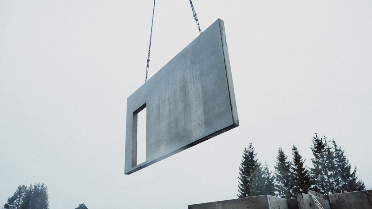 Bildet viser en byggeplass hvor et betongelement løftes av kran. 