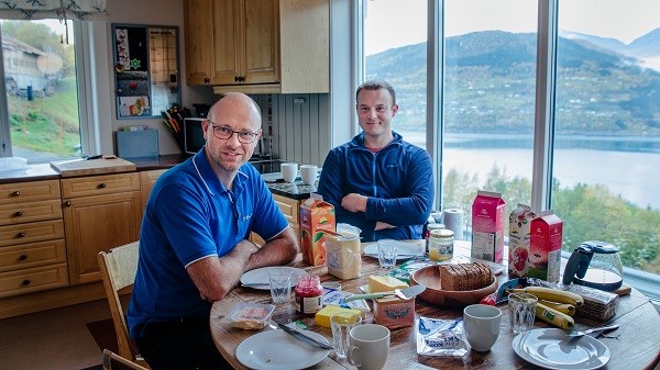 Jogeir Agjeld og Jan Markus Kvamm sit ved kjøkenbordet og et brødmat. Foto.