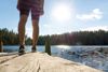 Bildet viser bein som står på ei brygge med skog og sol i bakgrunnen