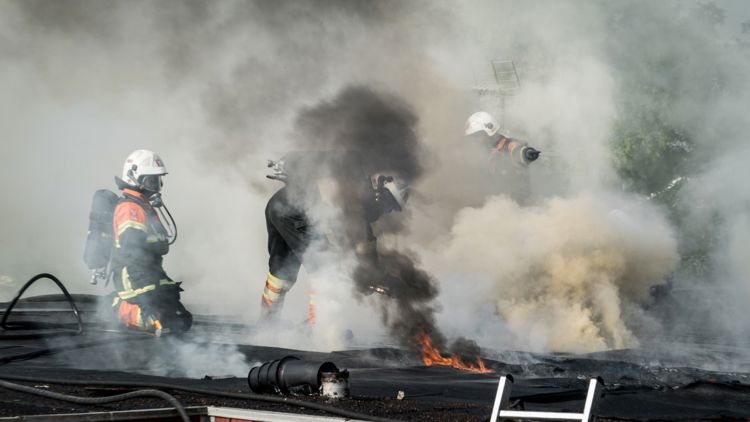 Illustrasjonsfotoet viser tre brannmenn i uniform med dykkermasker som prøver å slukke en brann.