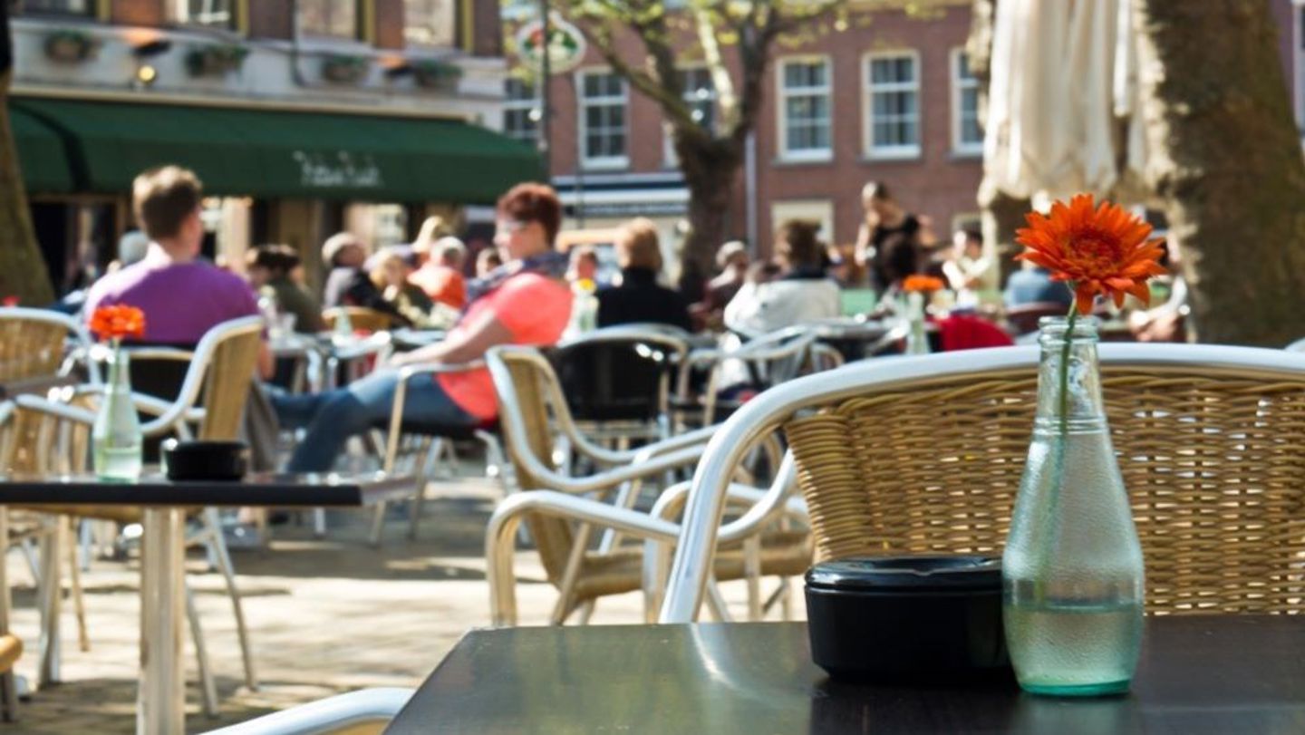 Bilde av mennesker som sitter ute på kafe i bakgrunnen, fokus på en vase på et kafebord