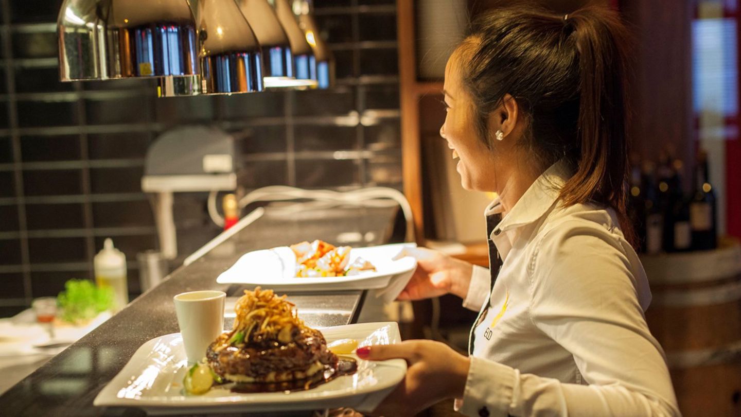 Bildet viser en kvinnelig servitør som bærer tallerkener i en restaurant. 